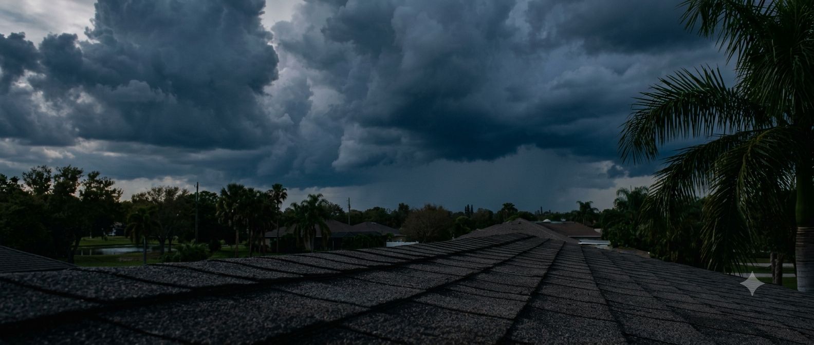 Dark storm clouds building over rooftops and palm trees before rain